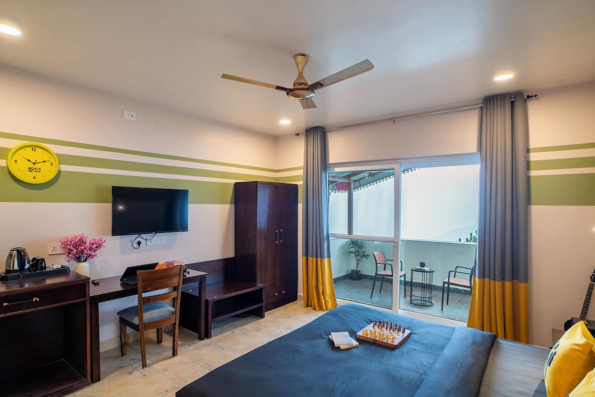Une chambre d’hôtel équipée d’un lit, d’un bureau, d’une chaise, d’une télévision et d’un balcon avec vue.