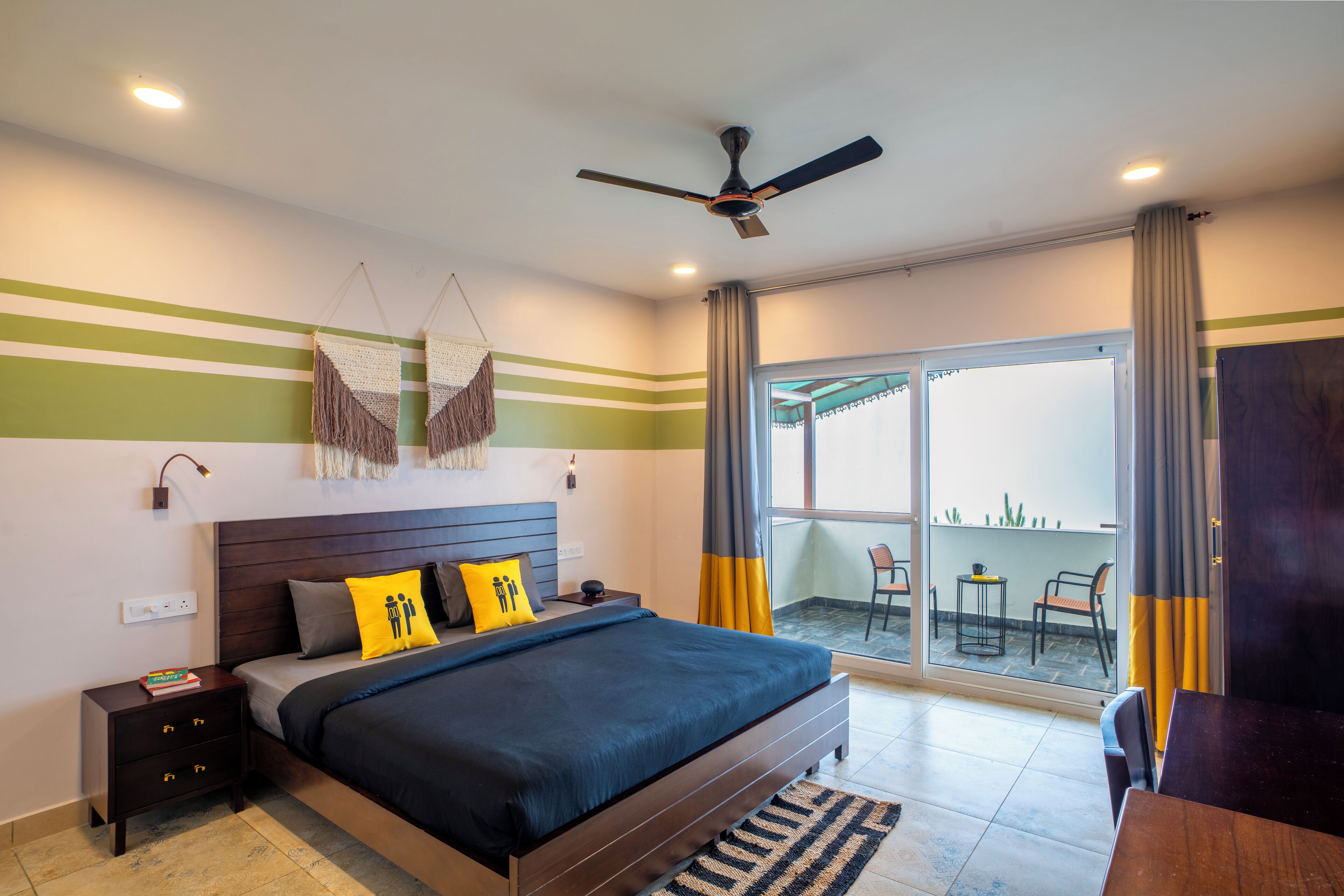 A modern hotel room with a large bed, a nightstand, a ceiling fan, and a view of the outdoor balcony.