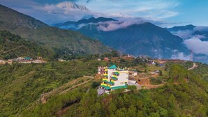 Um edifício de vários andares com telhado verde, cercado por vegetação exuberante e montanhas ao fundo.