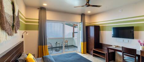 A hotel room with a bed, a desk, a chair, a TV, and a balcony with a table and chairs.