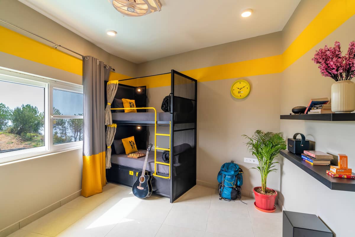 Une chambre avec un lit superposé, un bureau, une plante en pot et une fenêtre avec des rideaux.