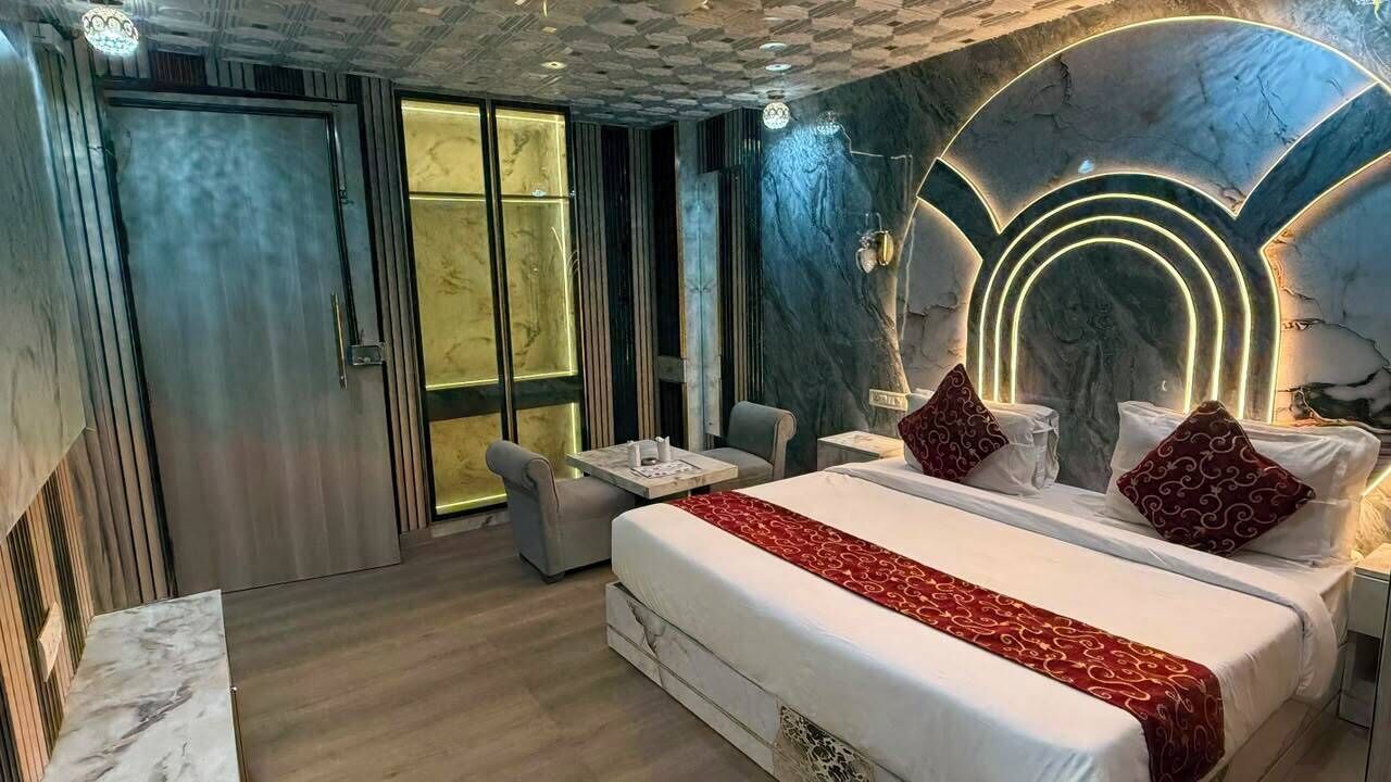 A modern hotel room with a bed, bedside tables, a seating area, and a marble wall with a light fixture.