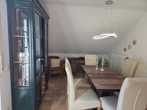 Un comedor con mesa de madera, sillas acolchadas, una vitrina de vidrio y una lámpara en el techo.