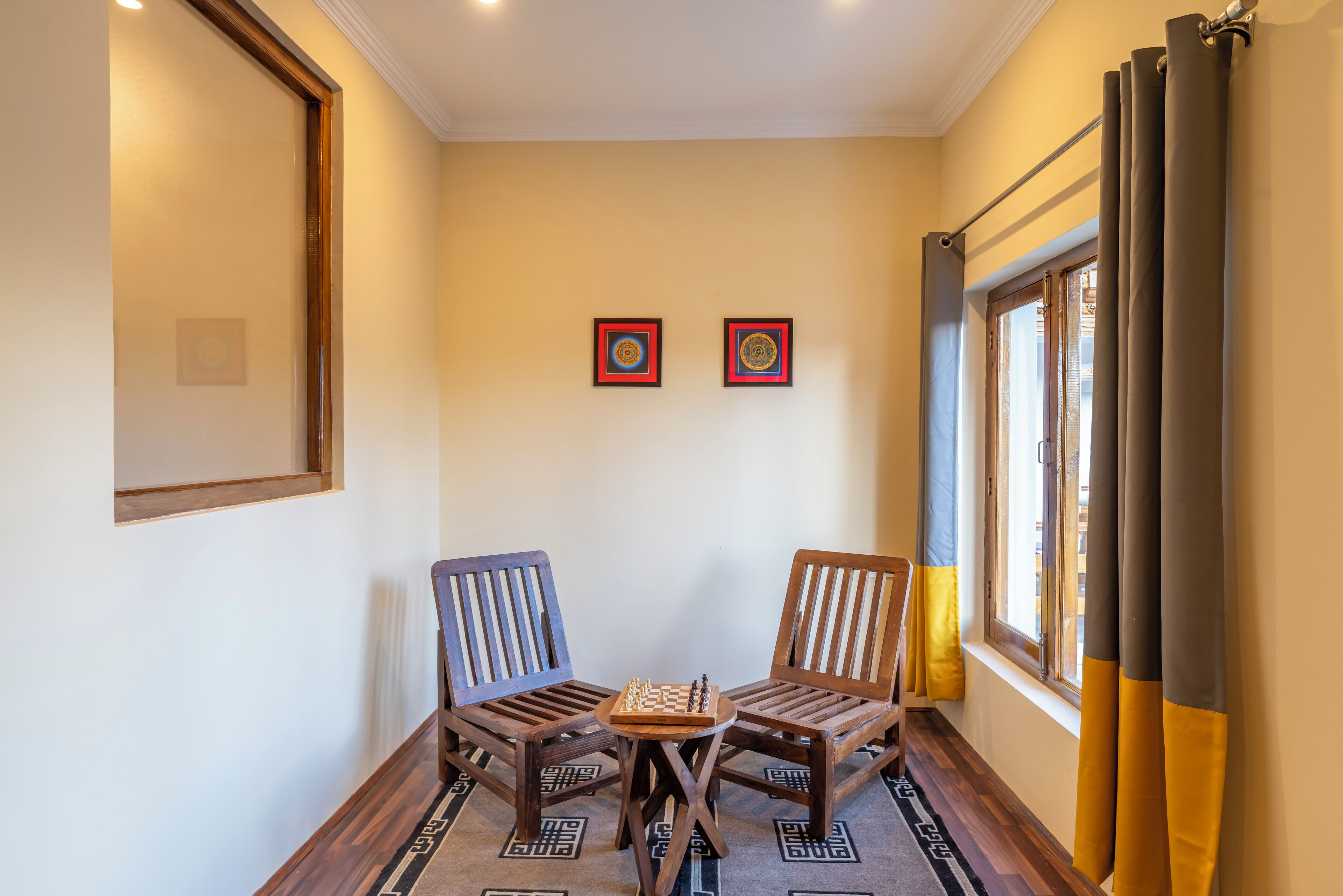 A room with two wooden chairs, a small table, and two framed artworks on the wall.