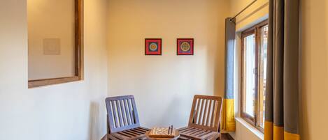 A room with two wooden chairs, a small table, and two framed artworks on the wall.