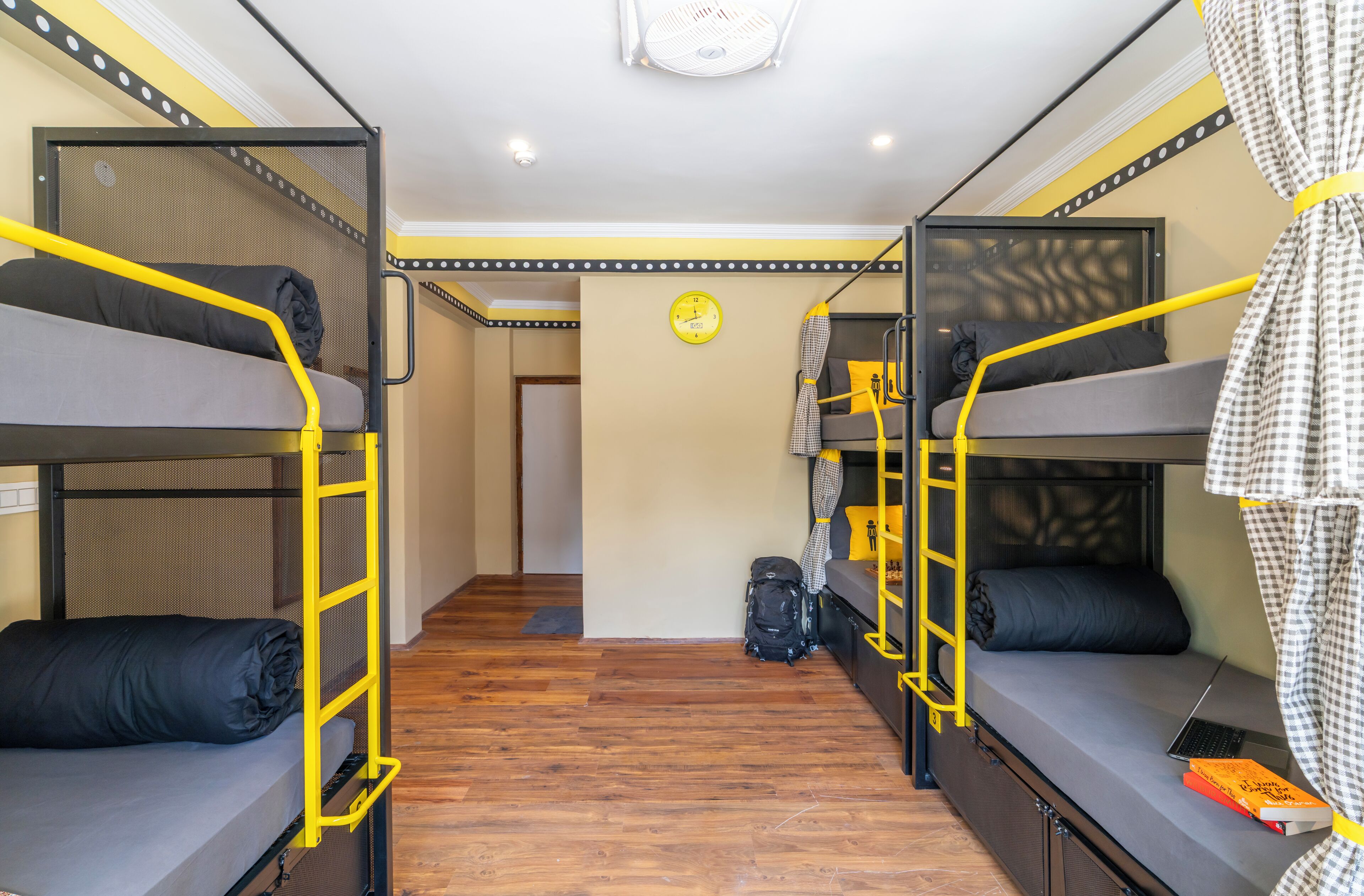 Een slaapkamer met een stapelbed, een houten vloer, een klok aan de muur en een koffer op de vloer.