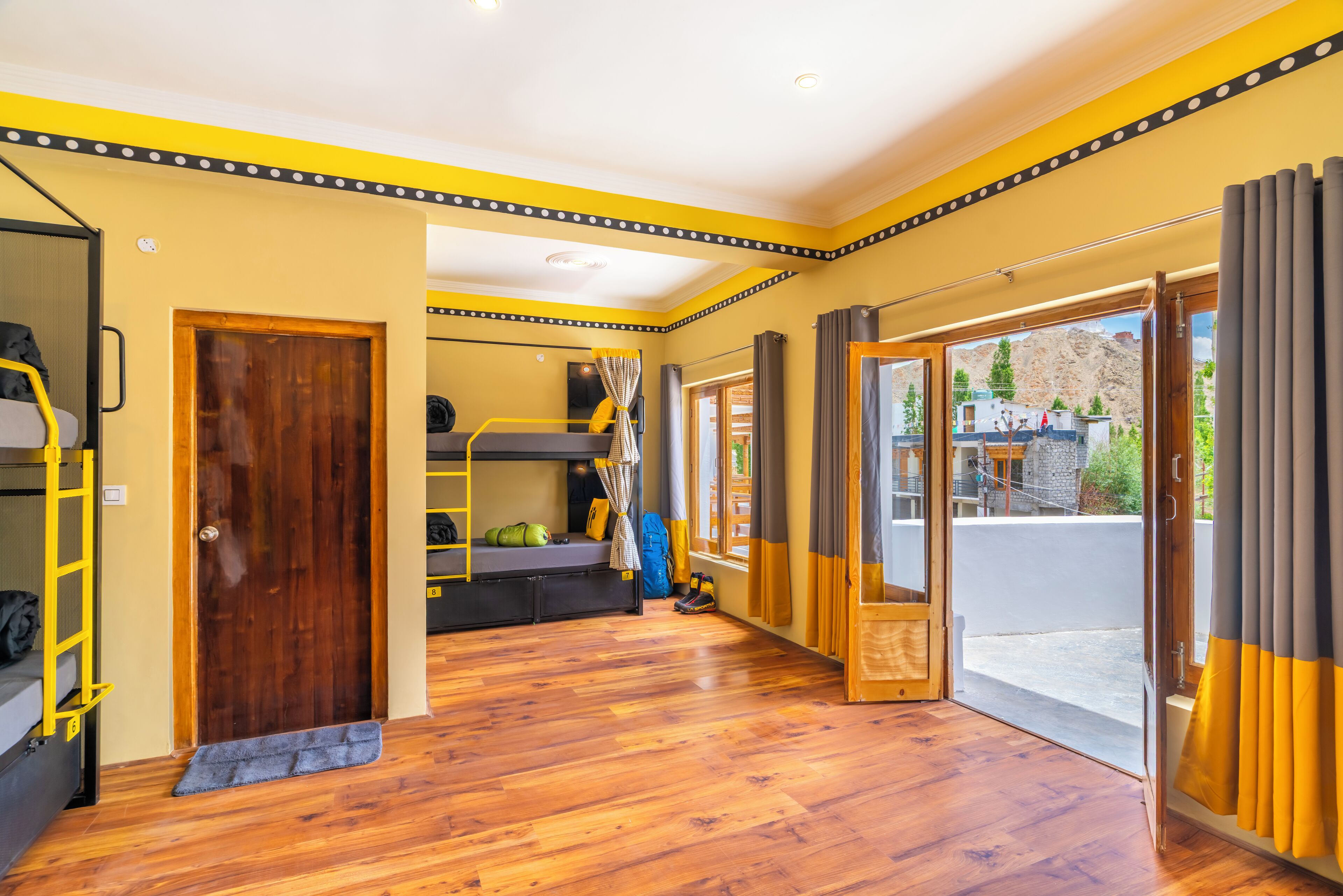 Une pièce avec un plancher en bois, un lit superposé, un bureau et une grande fenêtre avec des rideaux.