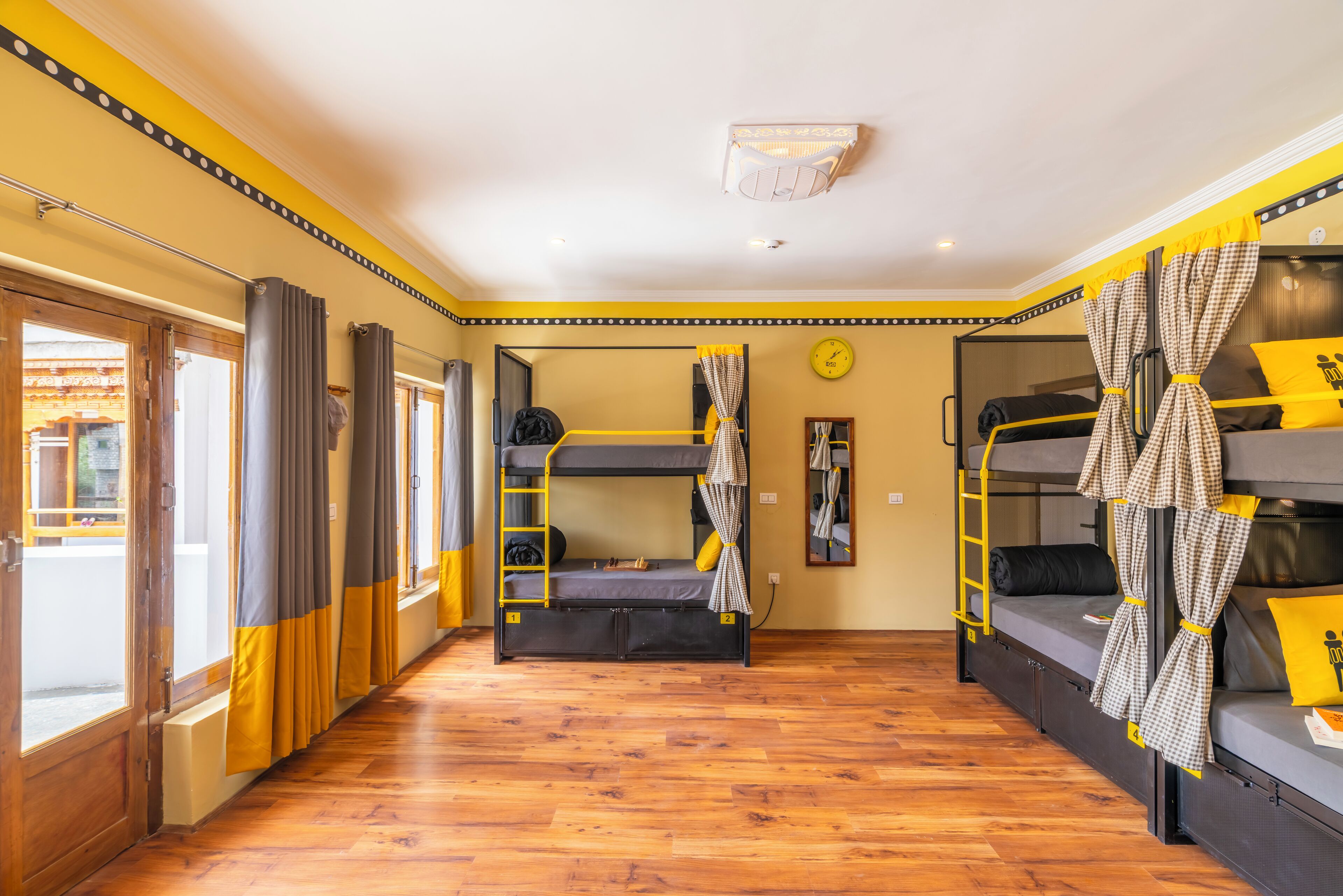 Una habitación tipo dormitorio con literas, suelo de madera, una ventana con cortinas y un reloj en la pared.