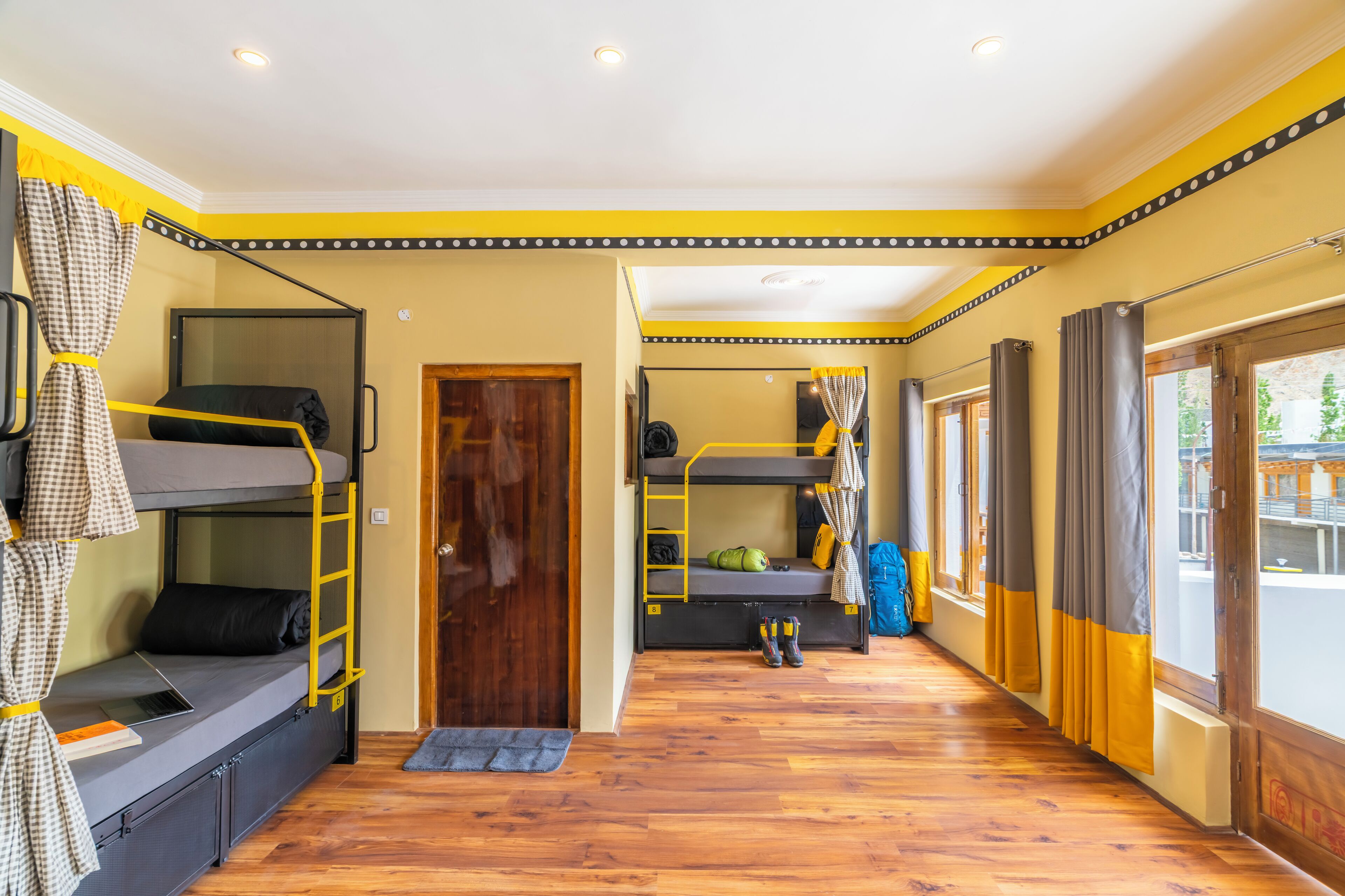 A room with bunk beds, a wooden floor, and a view through a window.