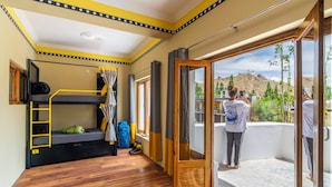 Ein Zimmer mit Etagenbetten, einer Leiter, einem mit Vorhängen versehenen Fenster und einem Balkon mit Bergblick.