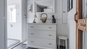A white dresser with drawers, a mirror, a basket with flowers, a cat statue, and a wooden sign with the word "Bastuy". - A house by the forest with a stream and plenty of peace and quiet (Stenis)