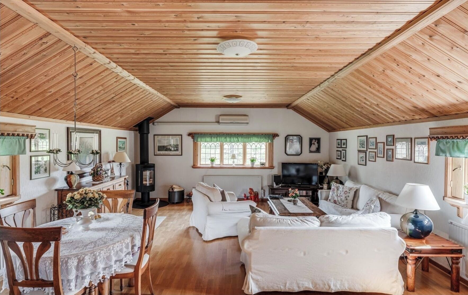 Ett mysigt rum med träpanel på väggarna, en öppen spis, en matplats och ett vardagsrum inrett med vita soffor och en tv.