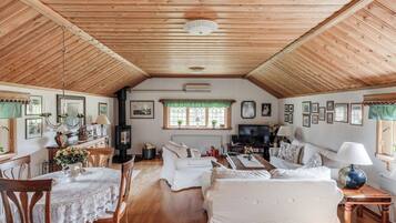 Una habitación acogedora con paneles de madera, chimenea, comedor y sala de estar amueblada con sofás blancos y un televisor.
