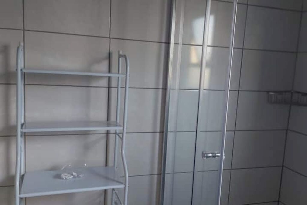 Ein Badezimmer mit weiß gefliesten Wänden, einem Metallregal und einer Duschkabine aus Glas.