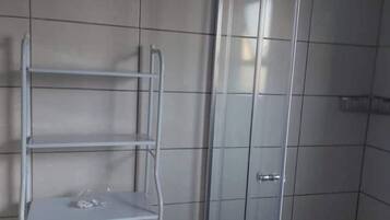 Ein Badezimmer mit weiß gefliesten Wänden, einem Metallregal und einer Duschkabine aus Glas.