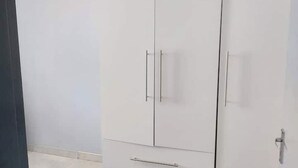 Ein weißer Kleiderschrank mit zwei Türen und einer Schublade, jeweils mit Griffen versehen.
