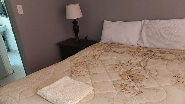 Cama bem arrumada com cabeceira acolchoada, luminária de mesa e travesseiro branco.