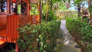 A wooden structure with a covered patio area, surrounded by lush greenery and a stone pathway. - Samran Resort (Chalong)