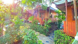 A wooden cabin with a thatched roof, surrounded by lush tropical vegetation and a stone pathway. - Samran Resort (Chalong)