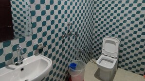 A bathroom with a checkered tile pattern, a sink, a toilet, and a shower. - Surya Residency (New Delhi)
