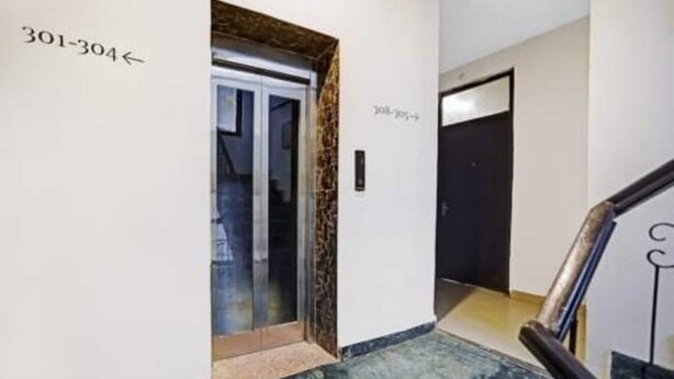 A hallway with a glass elevator door marked 301-304, a black door with a sign, and a marble floor. - Surya Residency (New Delhi)