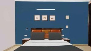 A bedroom with a blue accent wall, a wooden headboard, two bedside tables, and a bed with a white and orange bedspread. - Surya Residency (New Delhi)