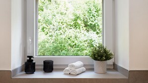 Una ventana con vistas a follaje, una planta en maceta y una toalla en un repisa.