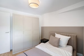 A bedroom with a bed, a wardrobe, a bedside table, and a ceiling light.
