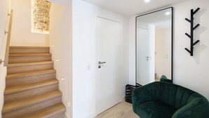 Una escalera lleva a una puerta blanca, una silla verde y un espejo grande en la pared.
