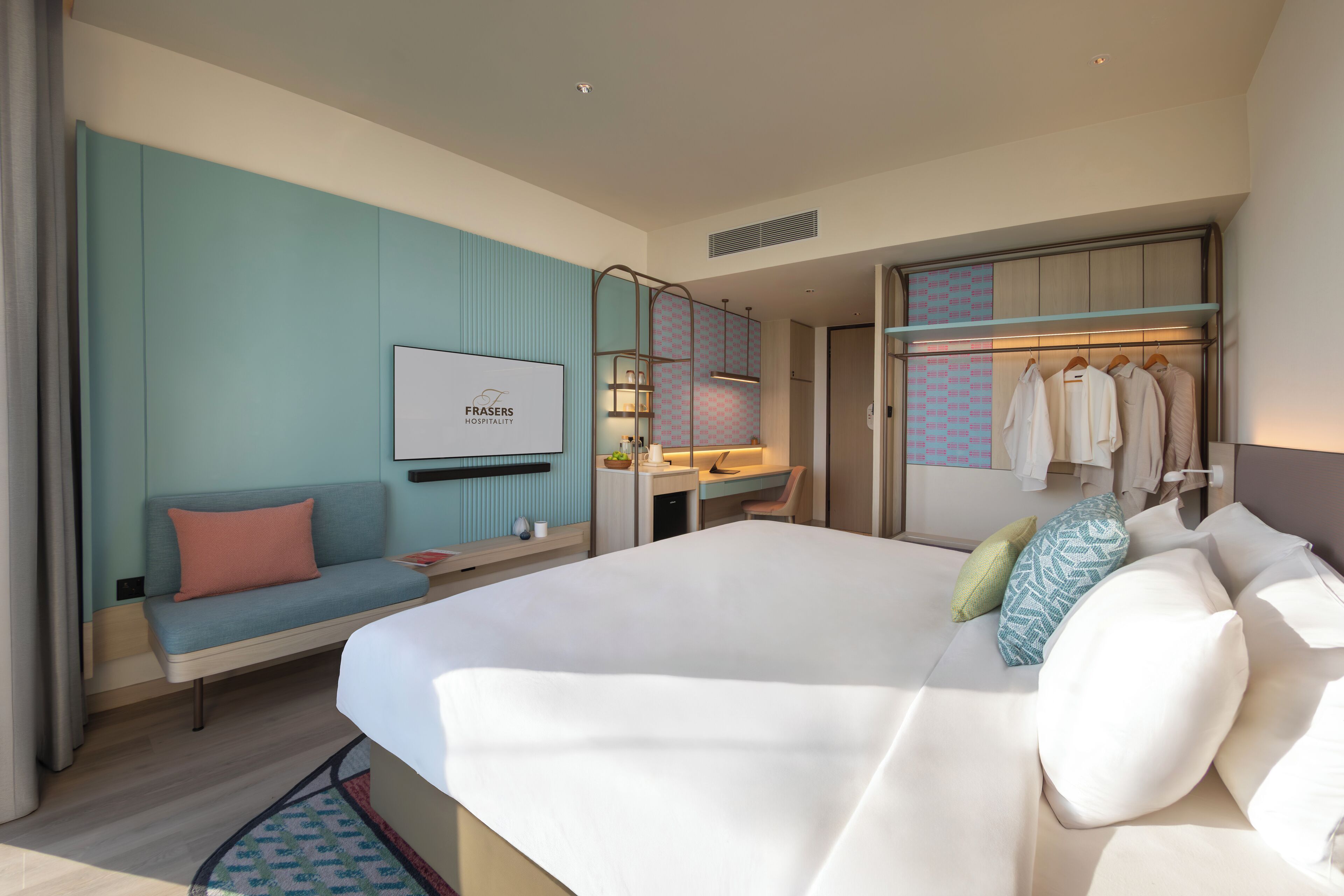 A modern hotel room with a large bed, a seating area with a sofa, a desk, and a wardrobe.