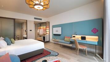 Habitación de hotel moderna con una cama grande, un escritorio con una computadora portátil, una zona de estar y un televisor en la pared.