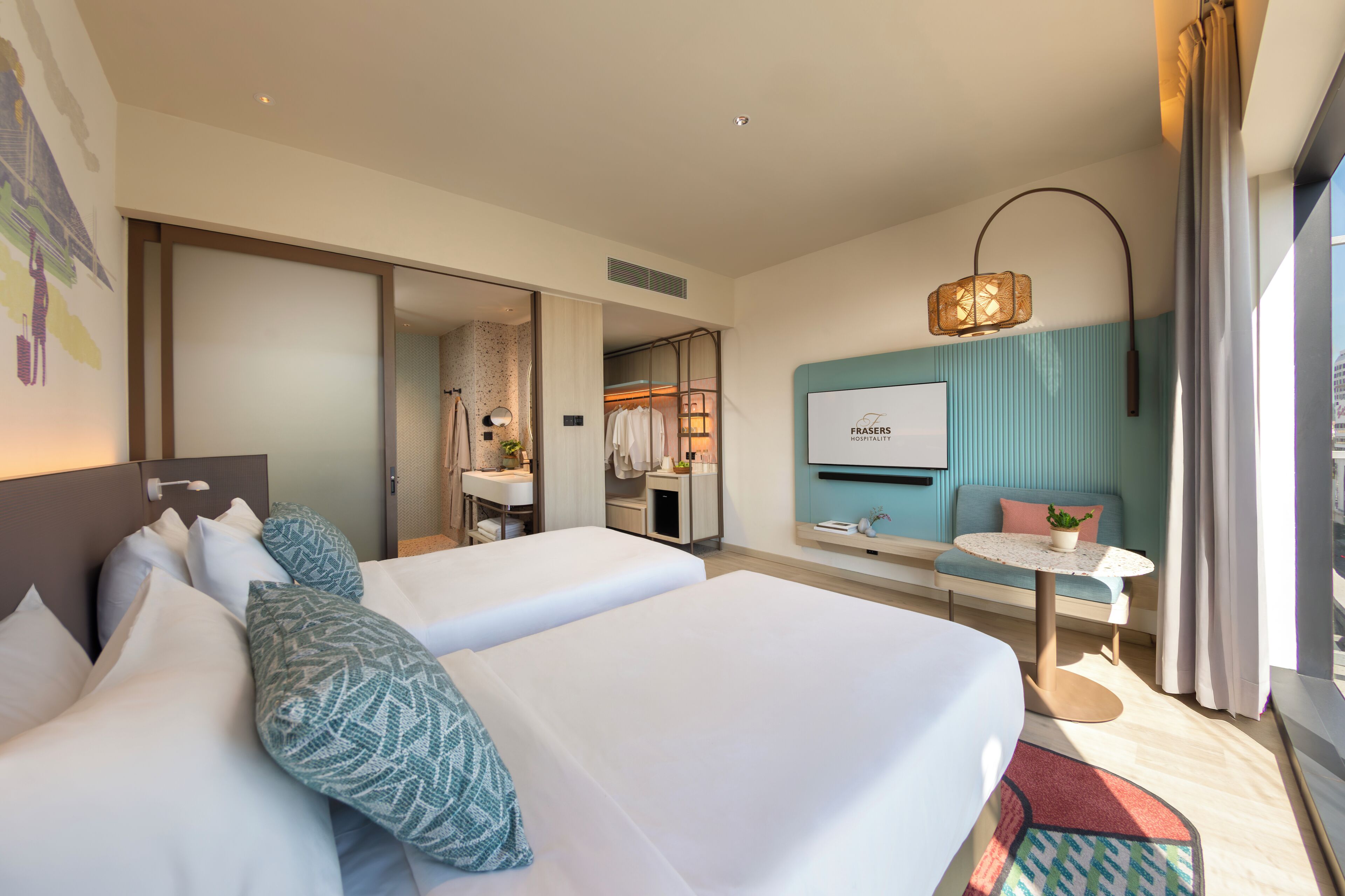 A hotel room with two beds, a small table, a TV, and a bathroom visible through an open door.