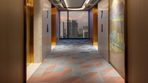 A modern elevator interior with a geometric patterned floor, a cityscape view through the windows, and a ceiling with recessed lighting. - Capri by Fraser Penang (George Town)