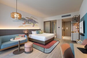 A modern hotel room with a bed, a sofa, a small table, and a desk with a laptop.