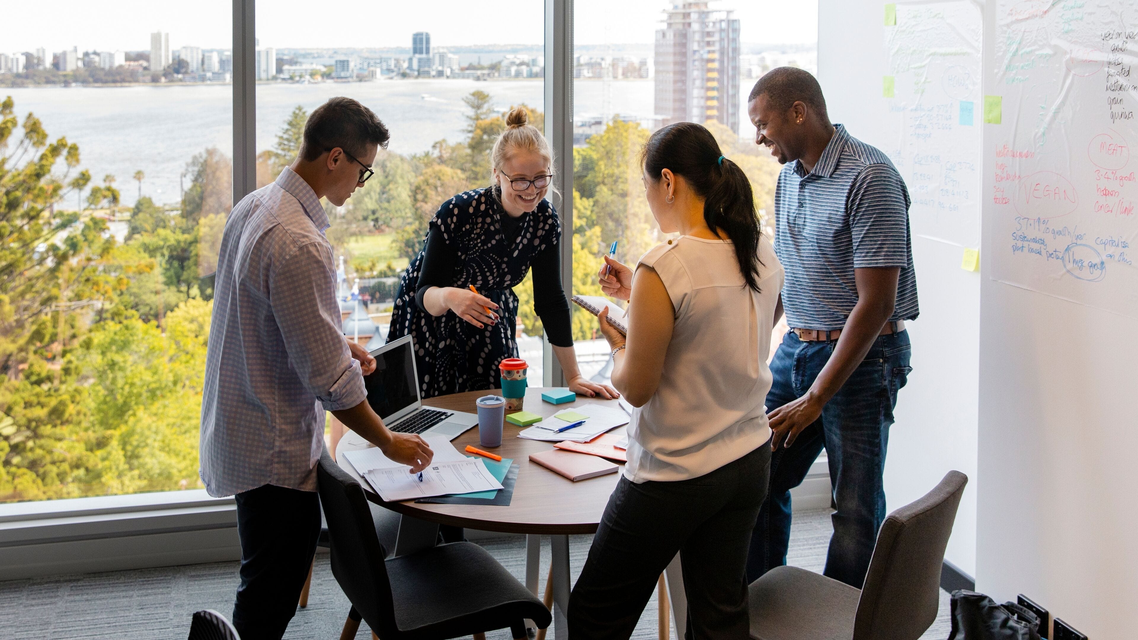 A group of people in a meeting room with a view of a cityscape and a river.