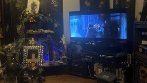 A living room with a television, a decorative plant, and a shelf with various items.