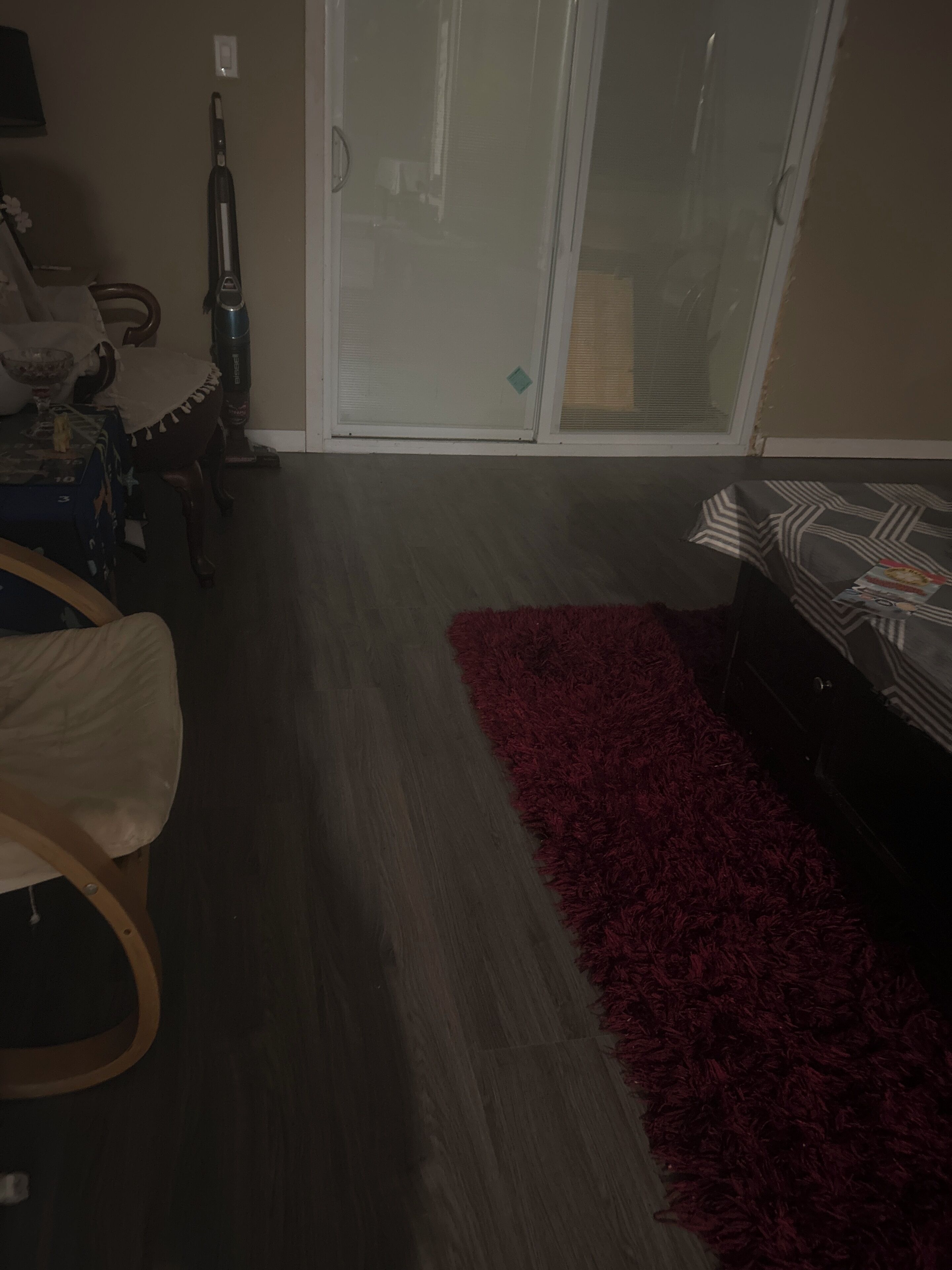 Une pièce dotée d’une porte-fenêtre coulissante, d’un tapis rouge, d’un plancher en bois, d’un lit avec une literie à motifs, d’une chaise et d’une table sur laquelle se trouvent un bol et une bouteille.