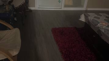 Une pièce dotée d’une porte-fenêtre coulissante, d’un tapis rouge, d’un plancher en bois, d’un lit avec une literie à motifs, d’une chaise et d’une table sur laquelle se trouvent un bol et une bouteille.