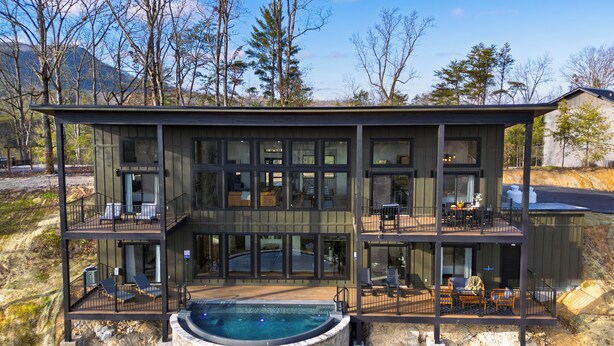 Ein modernes, mehrgeschossiges Haus mit großer Glasfassade, Außenbereichen zum Sitzen und einer Steinecke für eine Hot Tub.