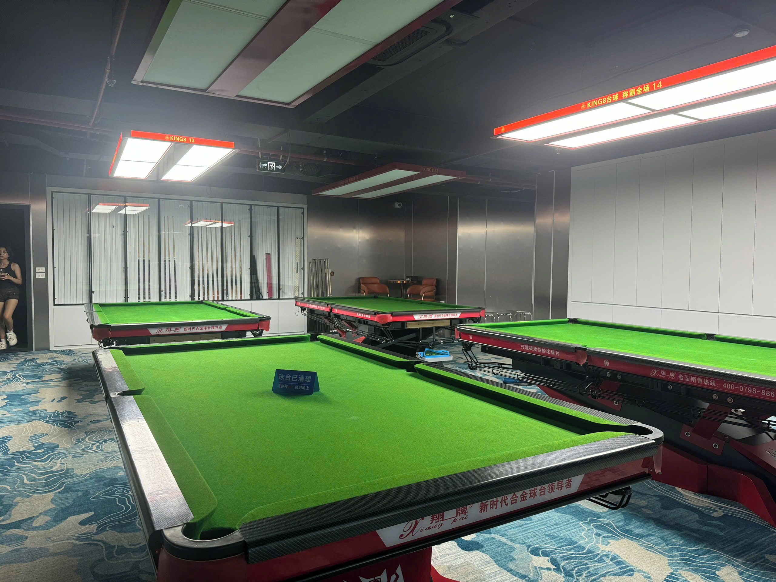 A billiards room with multiple tables, a pool cue rack, and a seating area.