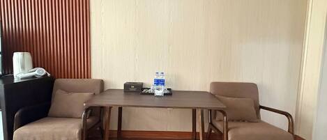 Una habitación con piso de madera, una mesa con dos sillas, una mesita auxiliar negra con un secador de pelo y una caja, y una pared de listones de madera.