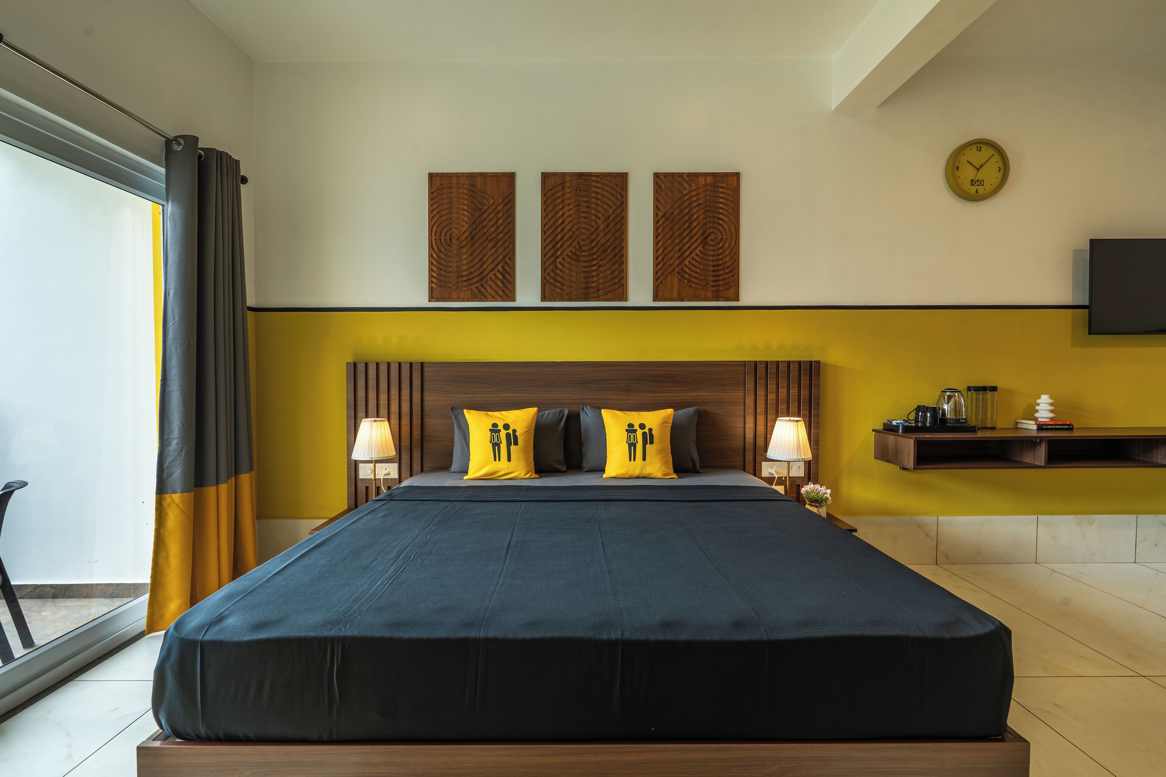 A modern hotel room with a large bed, two bedside lamps, a wall clock, and a TV mounted on the wall.