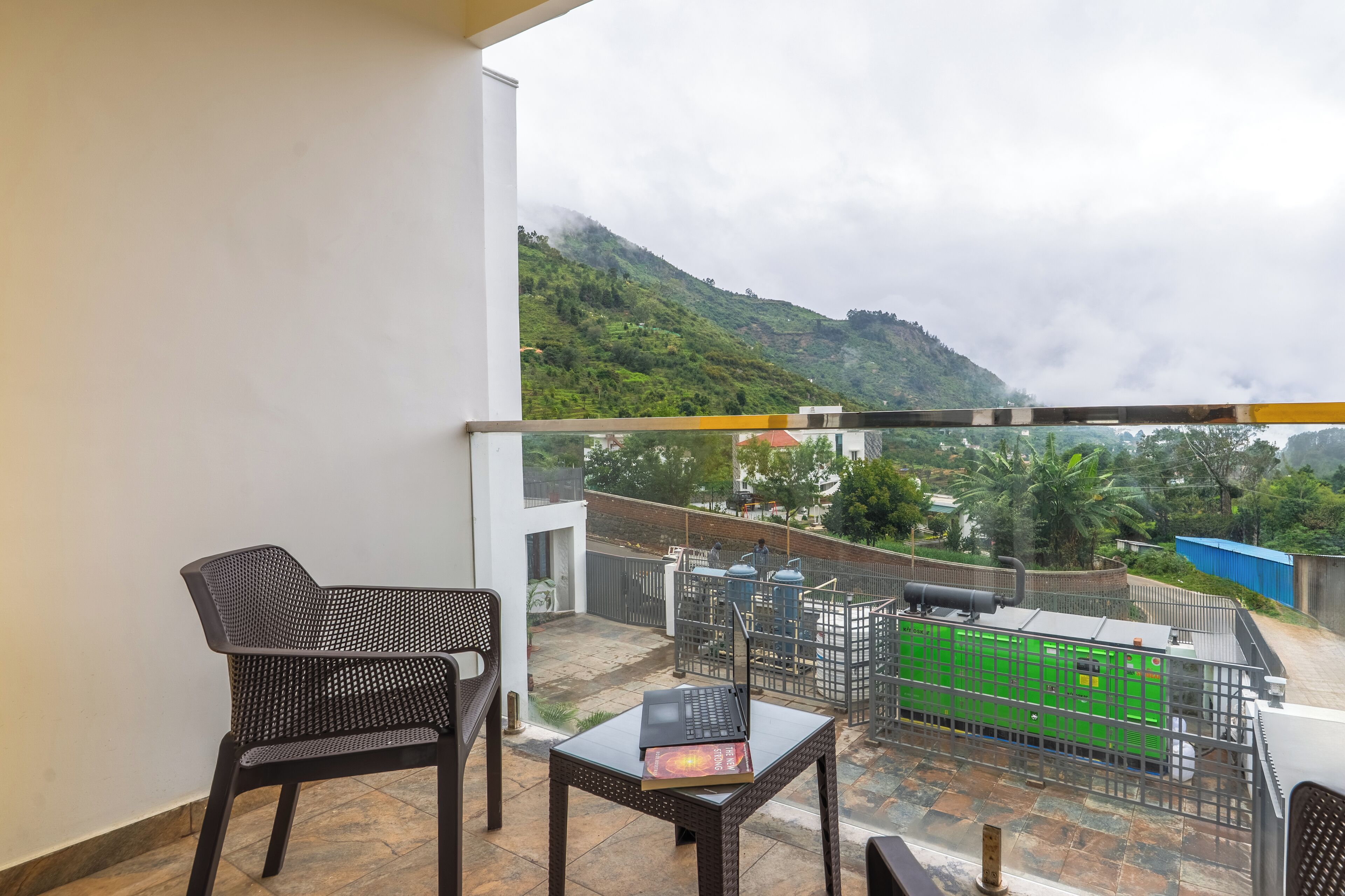 Un balcón con vistas a una colina verde, una mesa con una computadora portátil y dos sillas.