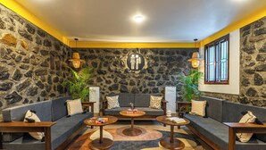 Un salon chaleureux avec un mur en pierre, un ensemble de canapés gris, des tables basses en bois et un grand tapis.