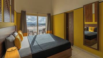 A hotel room with a bed, a view of the beach, and a balcony with chairs.