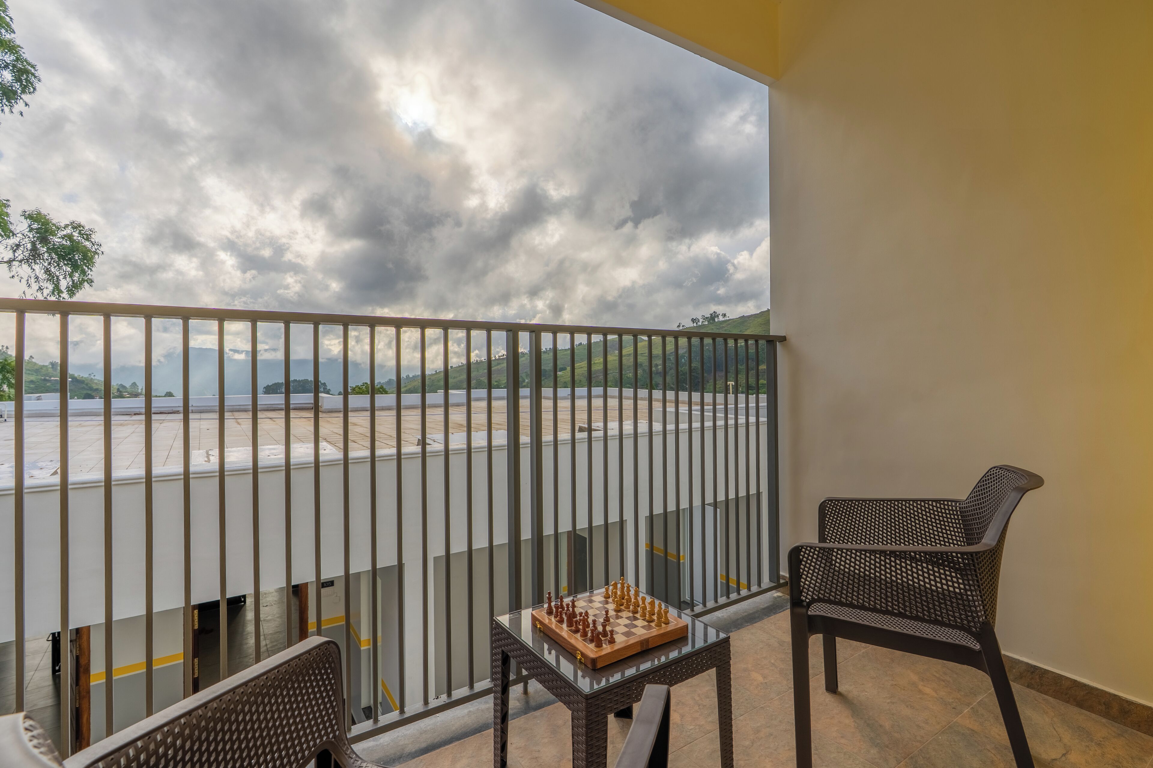 A balcony with a chessboard, a chair, and a view of a parking area and distant landscape.
