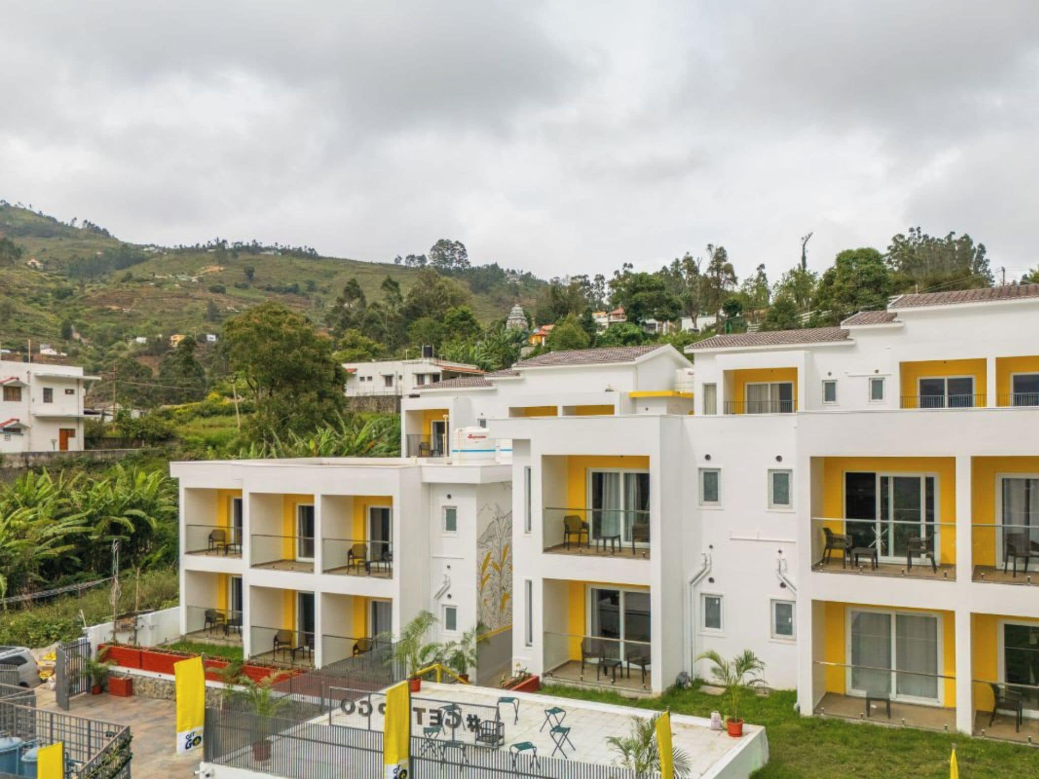 Un hotel de varios pisos con balcones, un patio interior y un paisaje montañoso al fondo.
