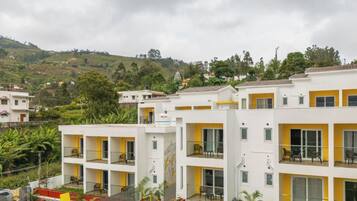 Un hotel de varios pisos con balcones, un patio interior y un paisaje montañoso al fondo.