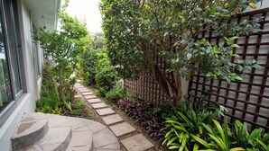 A stone pathway leading to a house with a wooden fence and lush greenery. - Echo garden apartment in Camps Bay (Cape Town)