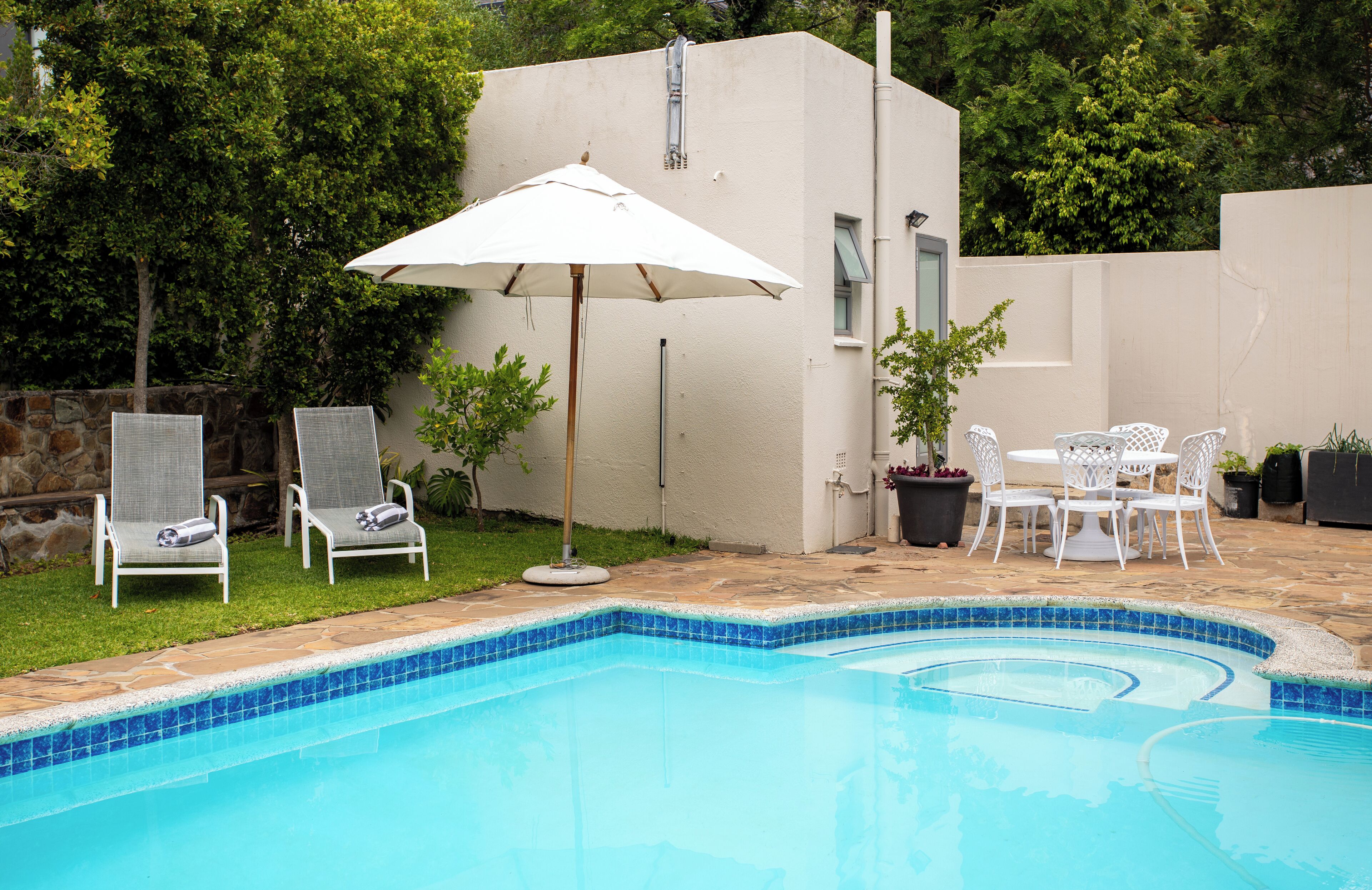 Ein Swimmingpool mit Liegestühlen und einem Tisch, umgeben von einer Steinmauer und viel Grün.